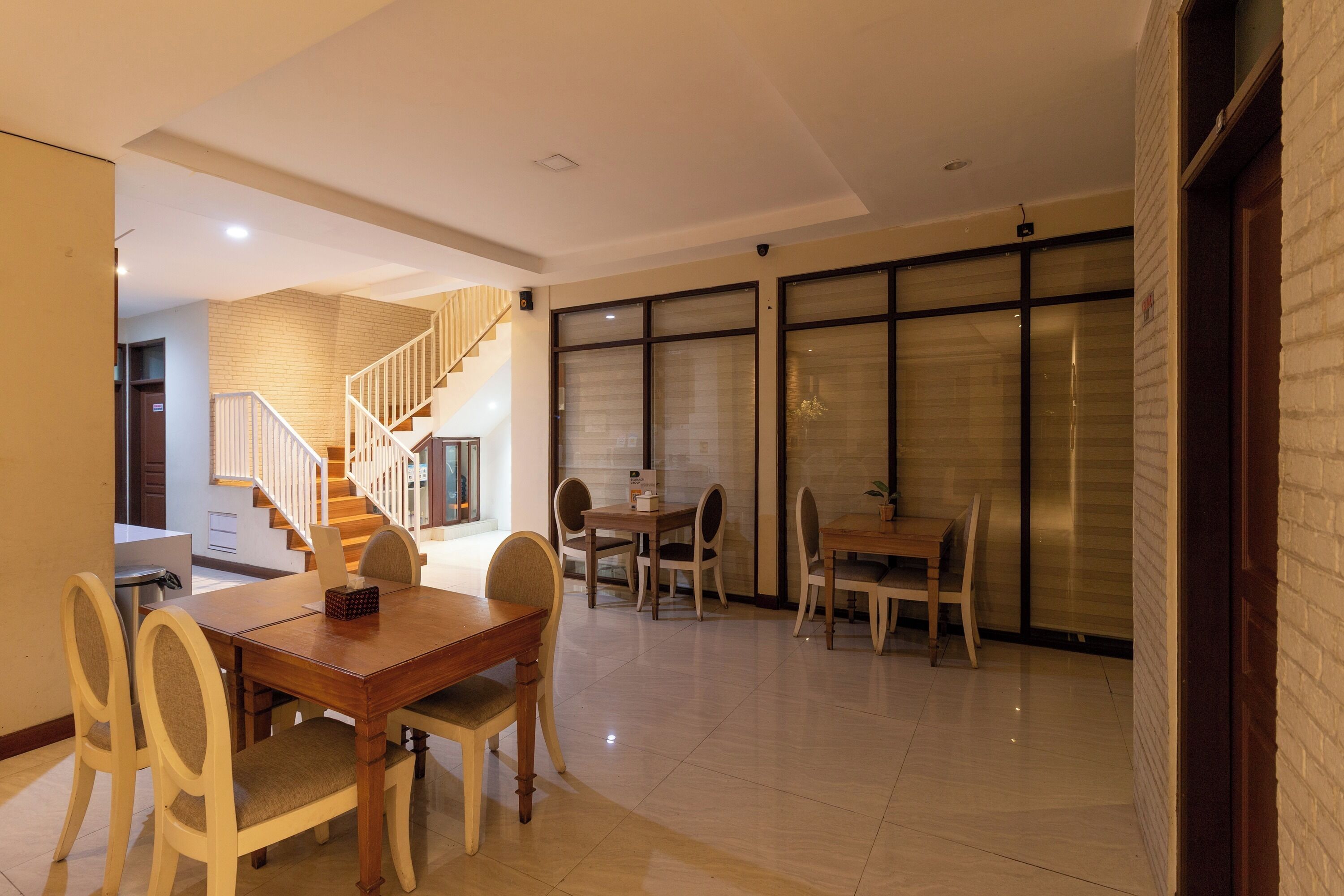 A spacious dining area with a wooden table and chairs, a staircase, and large windows with blinds.