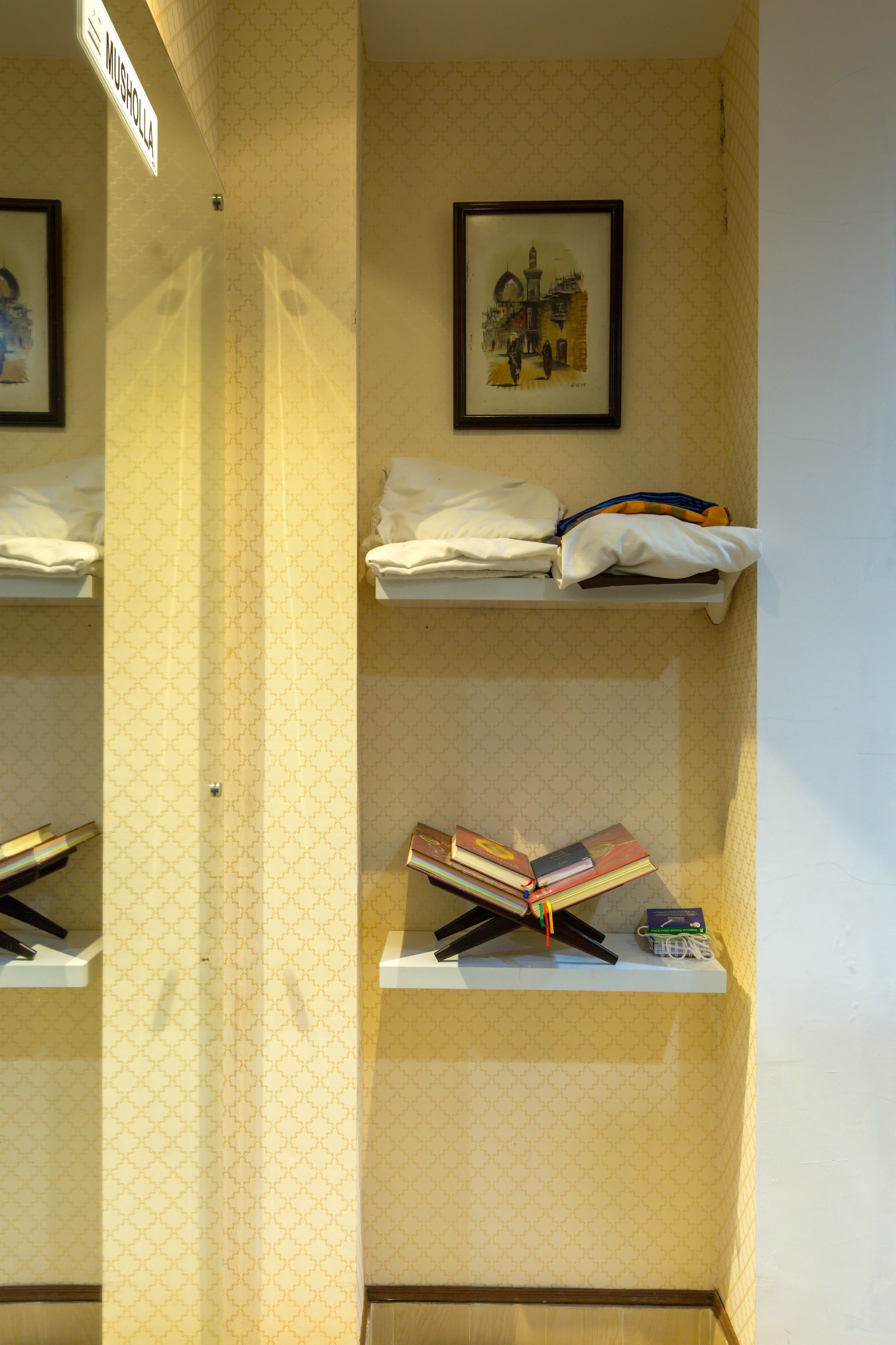 Une chambre d’hôtel avec un papier peint à motifs, un tableau encadré au mur, une étagère avec des serviettes pliées et une pile de livres.