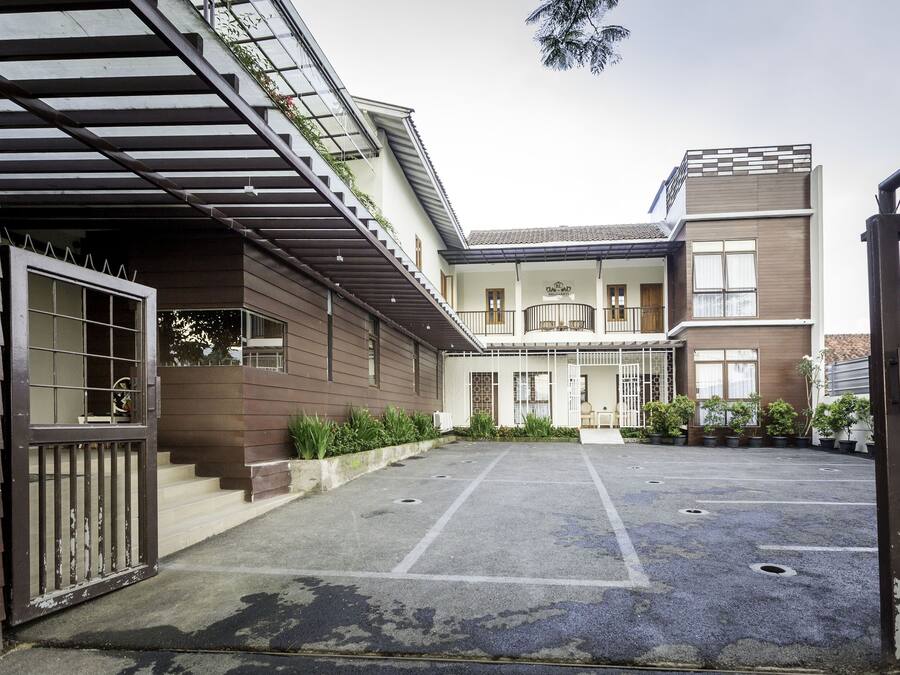 Un edificio de dos pisos con área de estacionamiento techada, entrada protegida por un portón y un balcón con plantas en macetas.