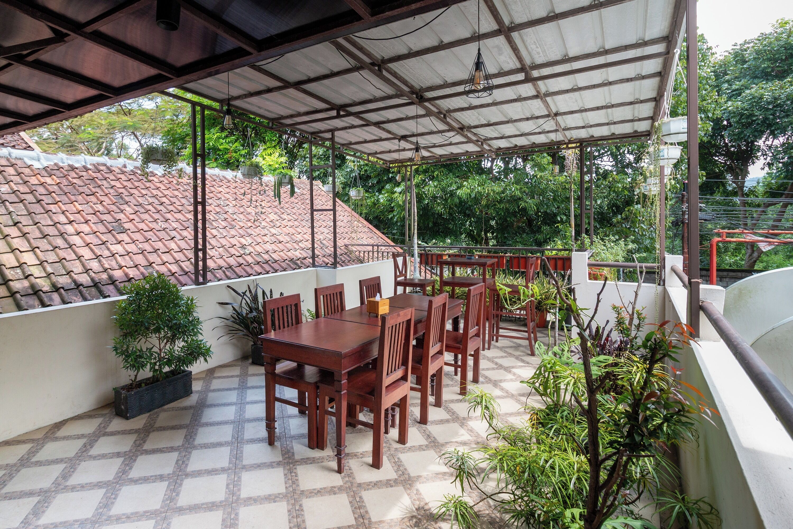 Un patio cubierto con suelo de baldosas, mesas y sillas de madera, y plantas en macetas.