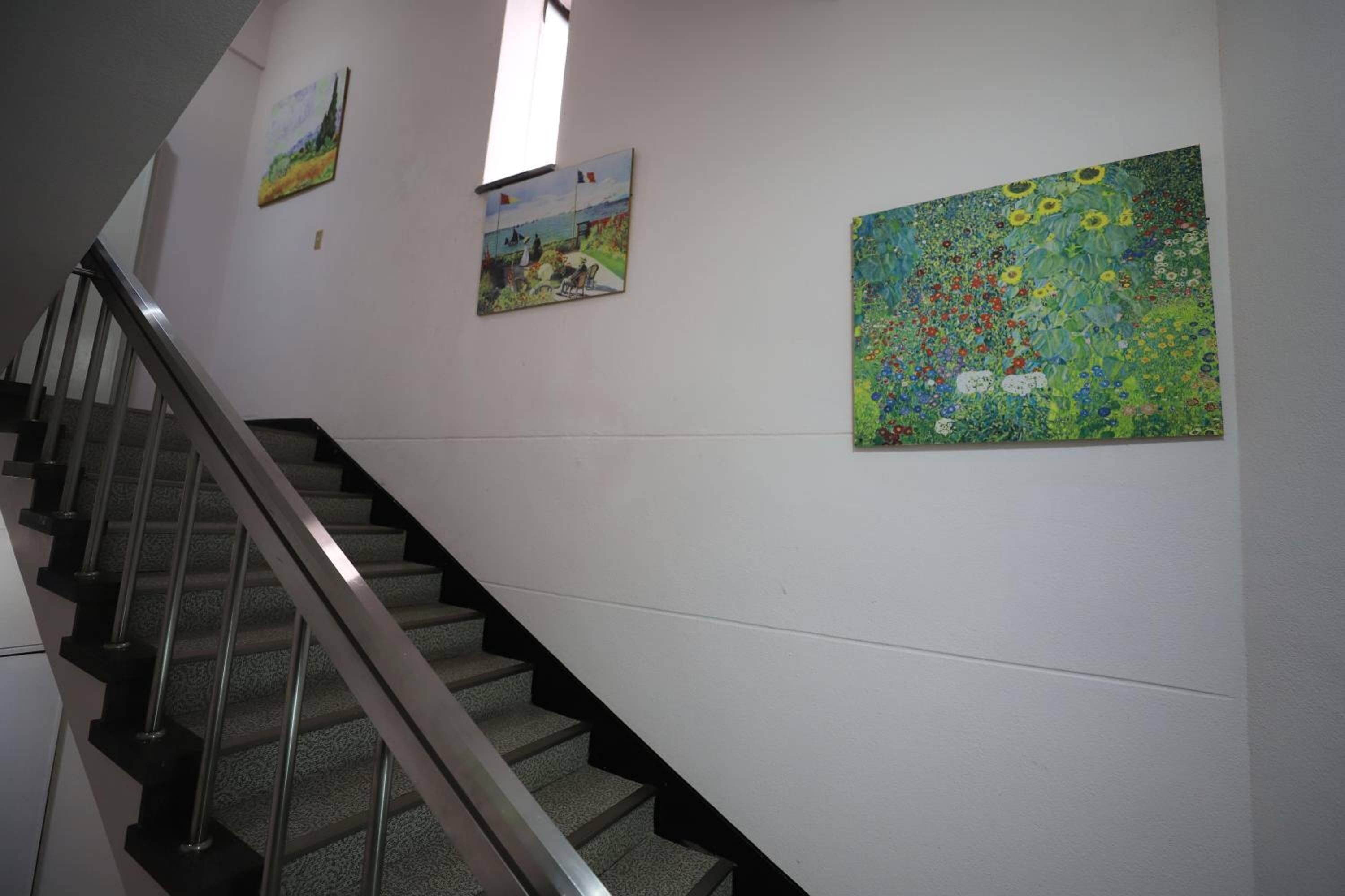 Una escalera con barandillas metálicas y una pared con tres cuadros.