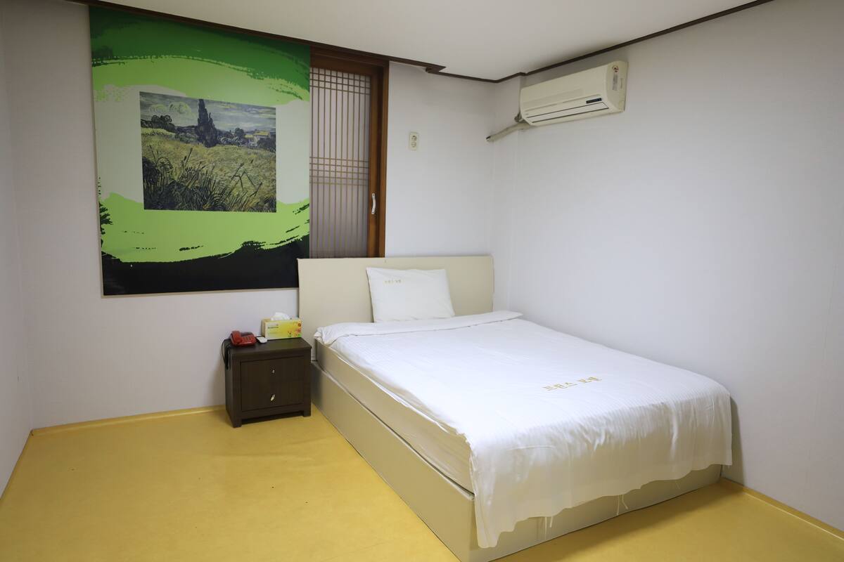 Un dormitorio con cama, mesita de noche, aire acondicionado en la pared y un cuadro.