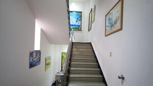 Una escala amb barana que condueix a un replà amb una porta. Hi ha obres d'art emmarcades a les parets.