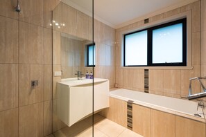 A modern bathroom with a glass shower enclosure, a white vanity with a mirror, and a window above the sink.