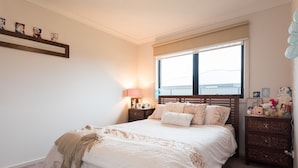 A bedroom with a bed, bedside tables, a window, and a shelf with pictures. - Euphoria House (Wynyard)