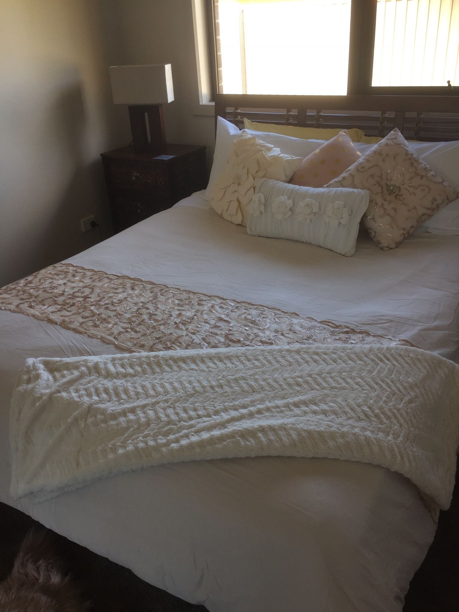 A neatly made bed with a decorative throw, pillows, and a bedside lamp.