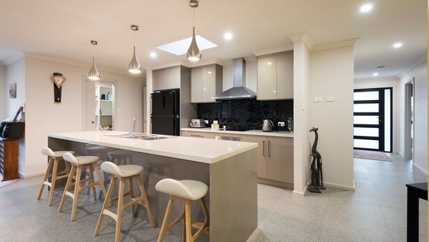 A modern kitchen with a central island, bar stools, pendant lighting, and a black backsplash. - Euphoria House (Wynyard)