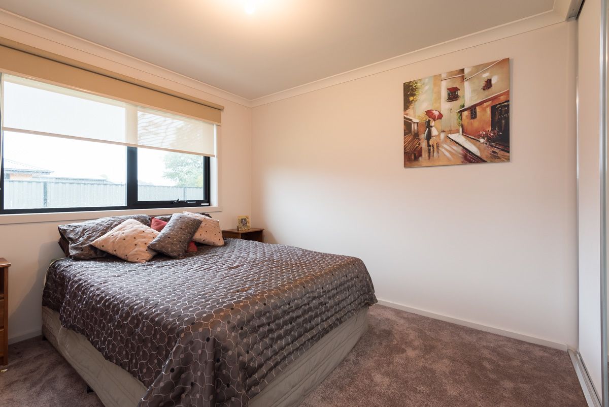 A bedroom with a bed, a nightstand, a window with blinds, and a painting on the wall.