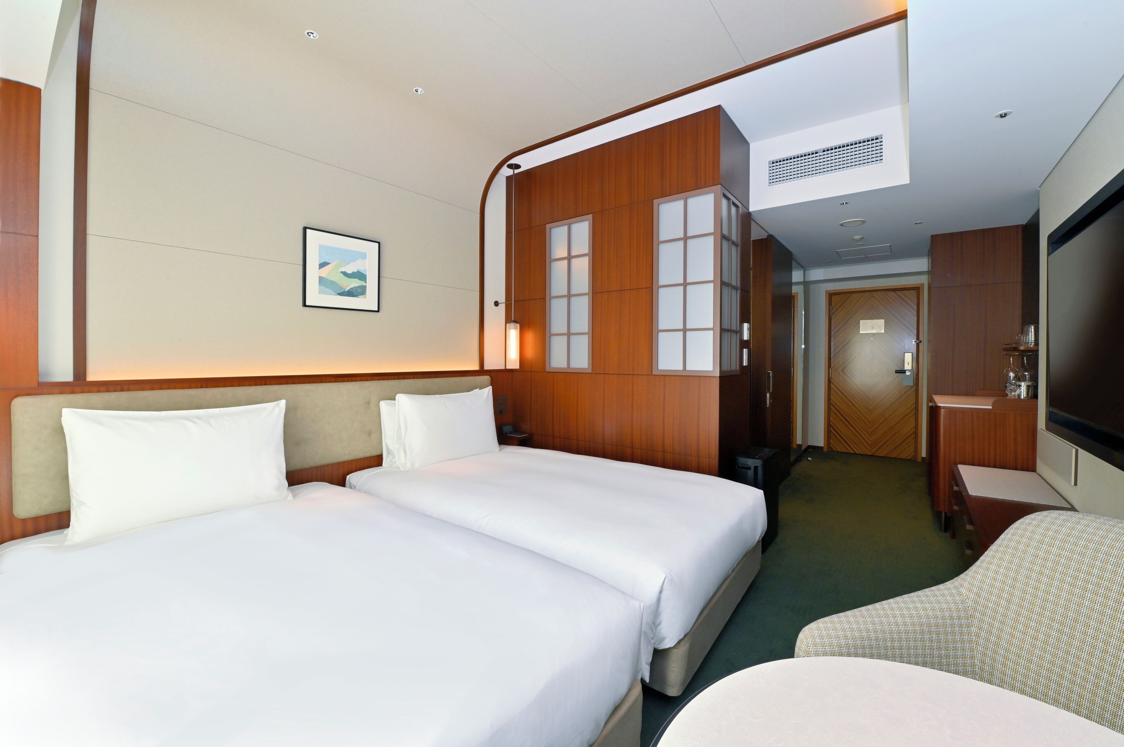 Quarto de hotel com duas camas, uma escrivaninha, uma cadeira e uma televisão.