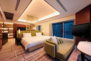A hotel room with a bed, sofa, TV, and a large window with a city view.