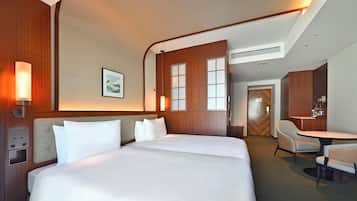 A hotel room with a large bed, a desk, and a chair. There is a wall-mounted control panel and a picture on the wall.