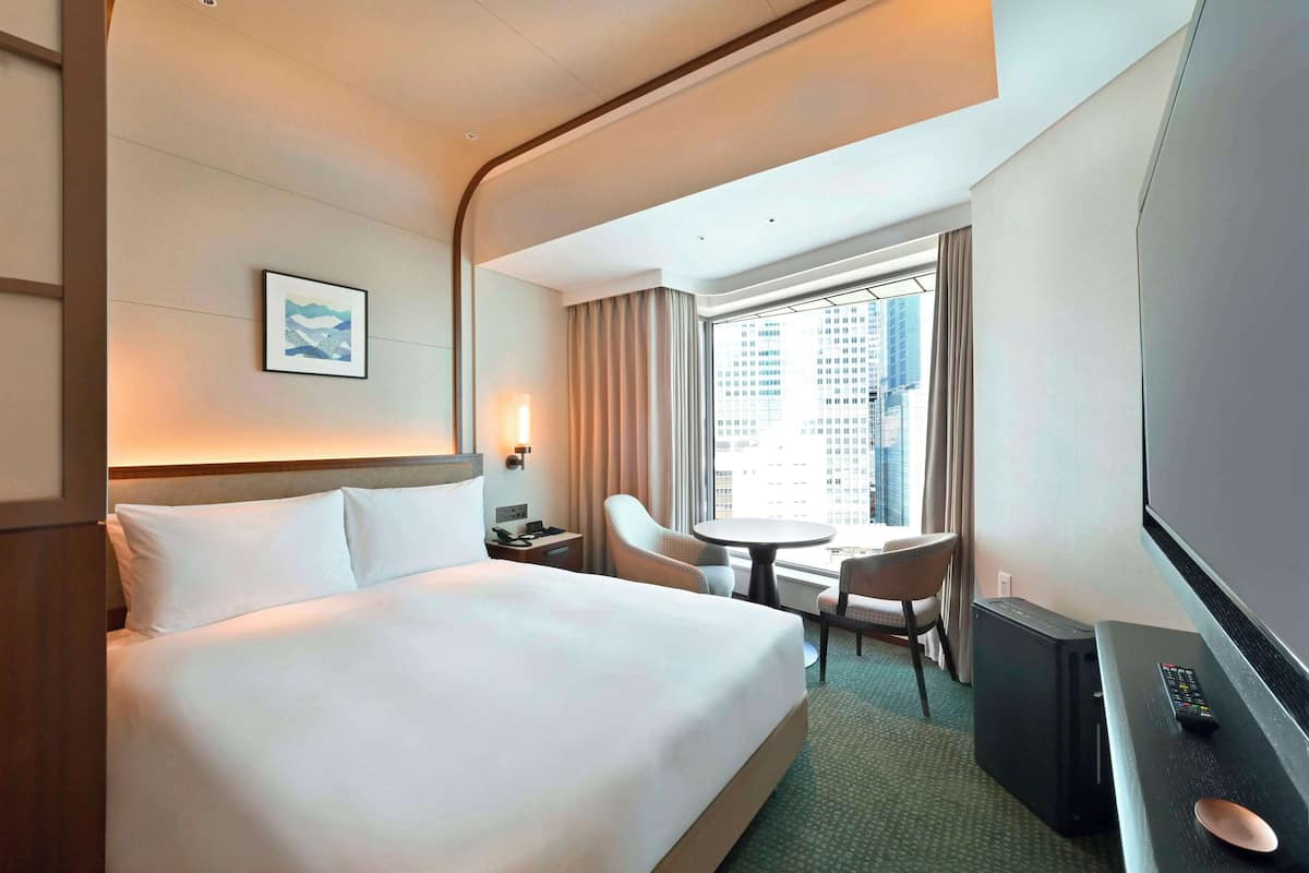 A hotel room with a large bed, a desk with a computer, a chair, a small table, and a TV.