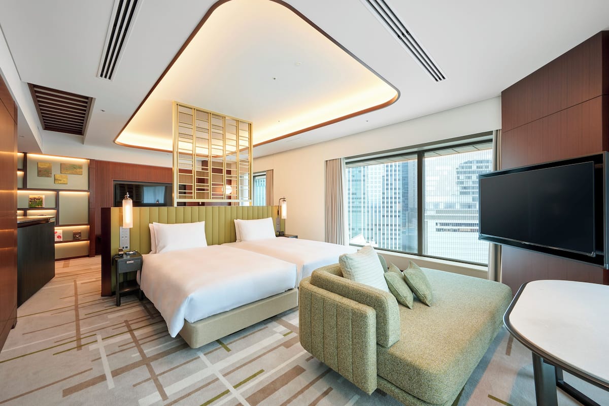 A hotel room with two beds, a sofa, a TV, and a city view.