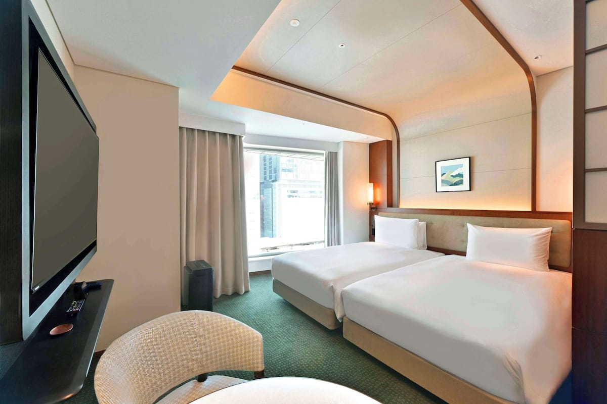 A hotel room with two beds, a TV, a desk, and a window with curtains.
