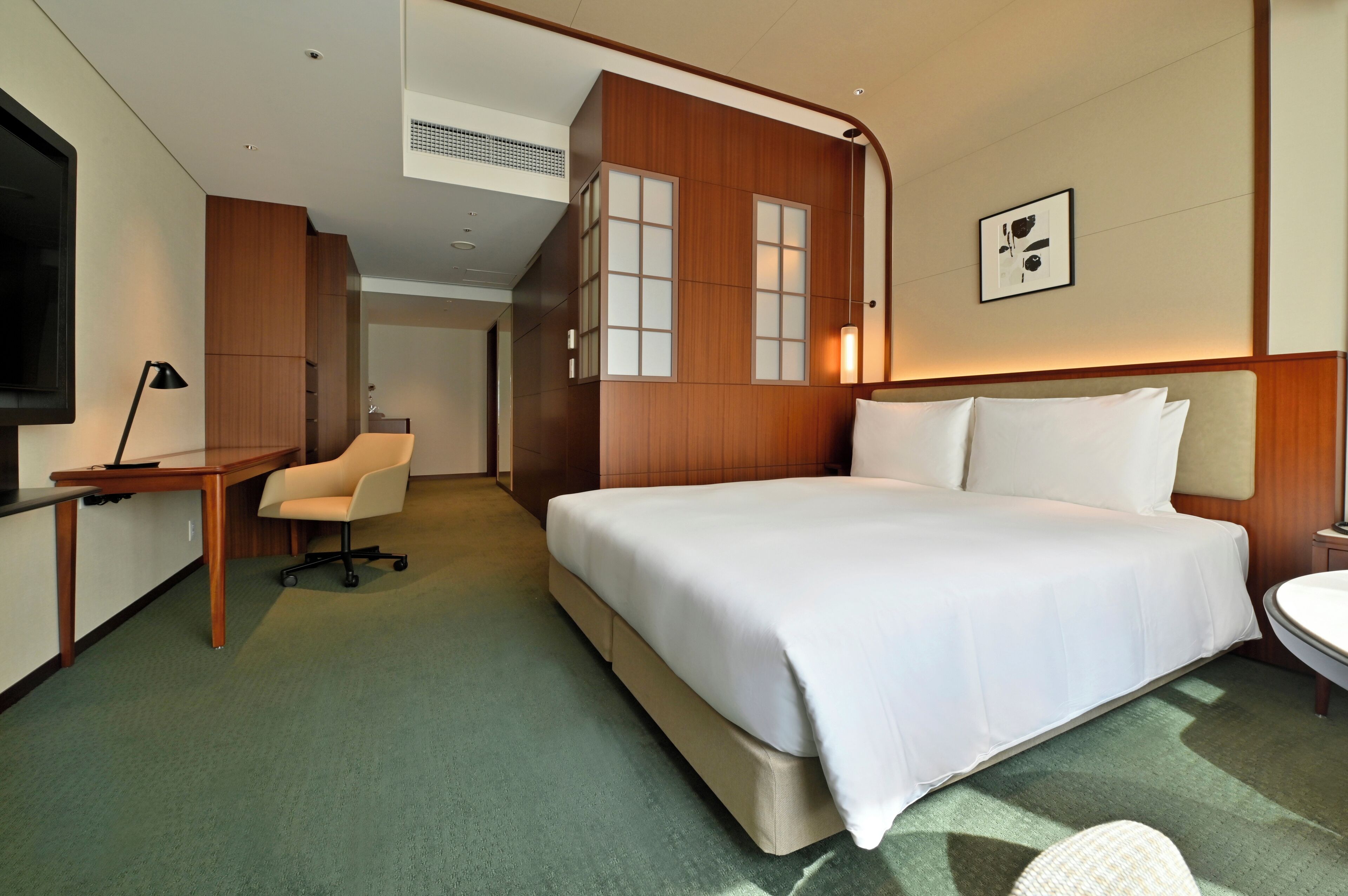 A hotel room with a large bed, a desk, a chair, a TV, and a bathroom.