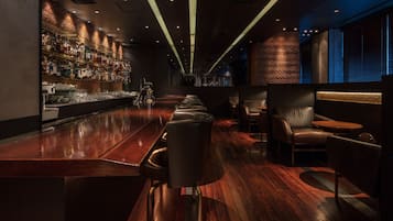 A bar area with a long counter, bar stools, and a brick wall.