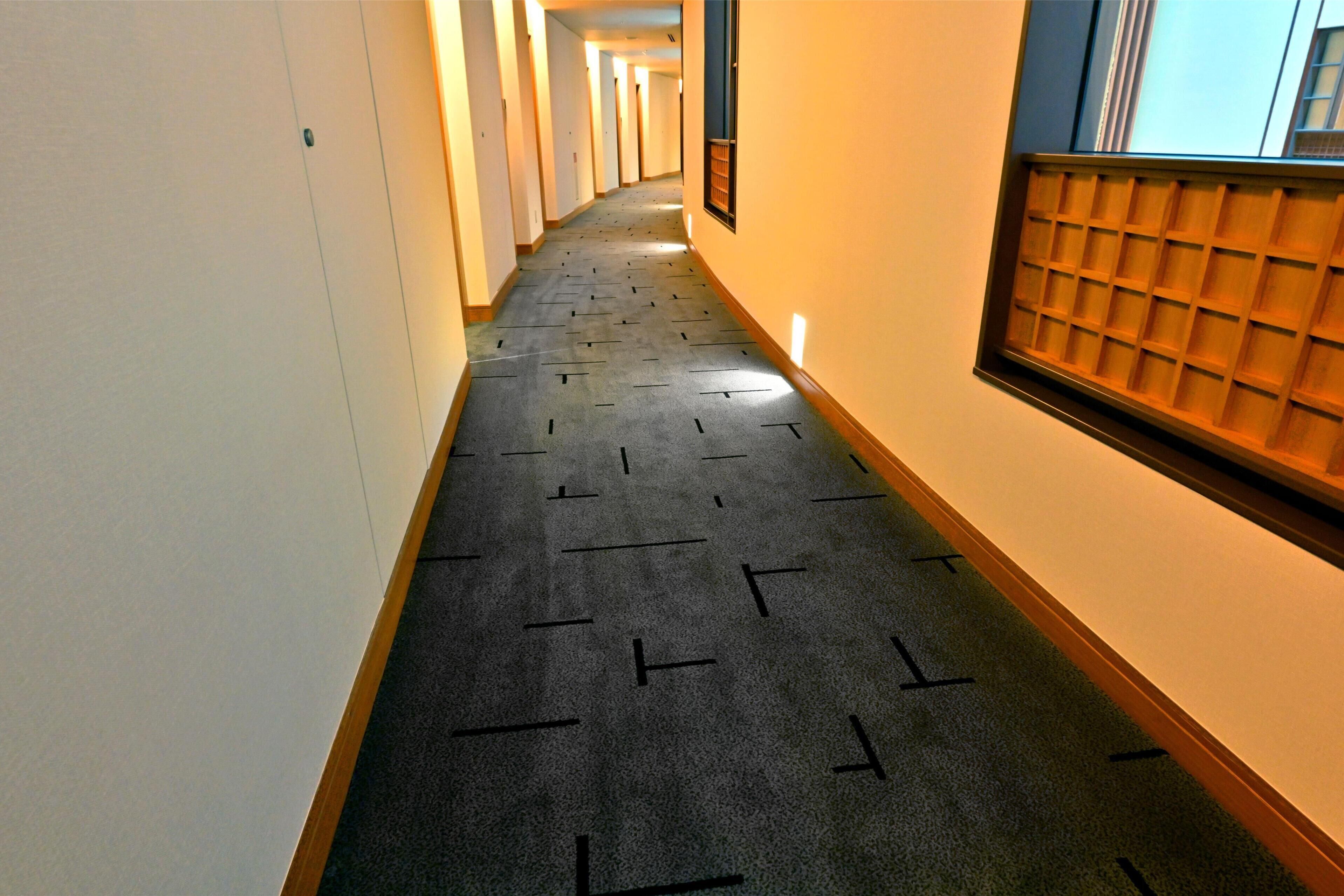 A hallway with a patterned carpet, white walls, and a wooden-framed window with a grid pattern.