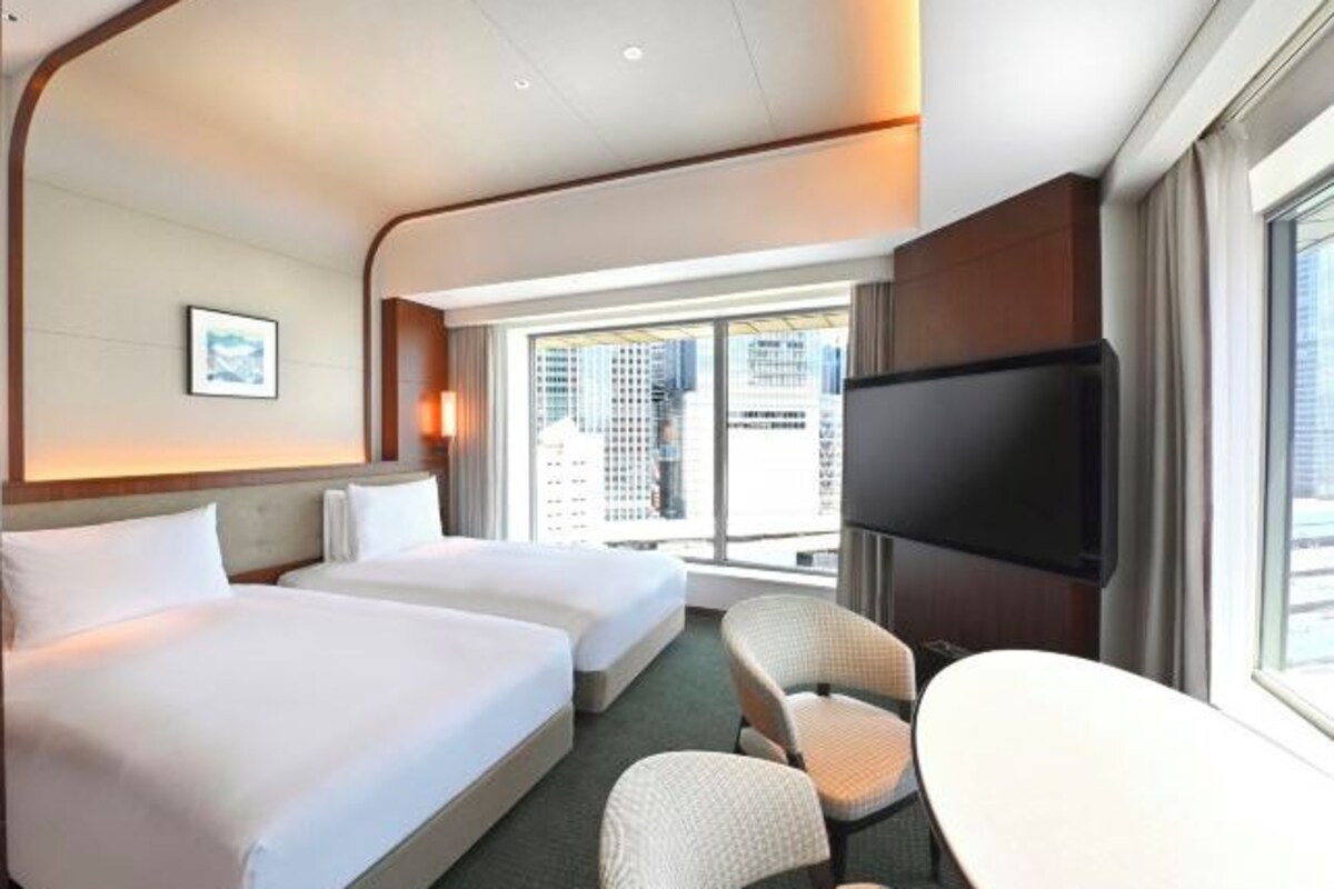 Une chambre d’hôtel avec deux lits, un téléviseur à écran plat, une table à manger et une vue sur la ville.