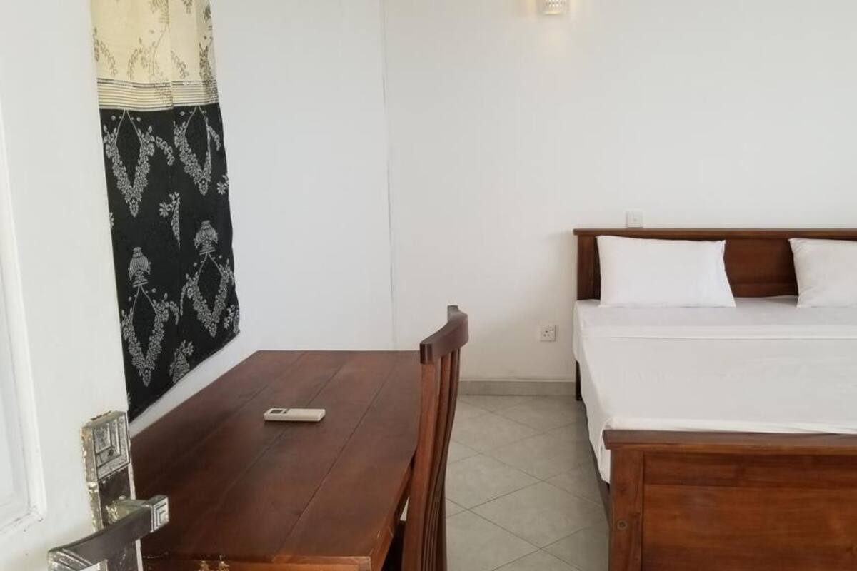A bedroom with a wooden bed, white bedding, a wooden table, and a patterned tapestry on the wall.