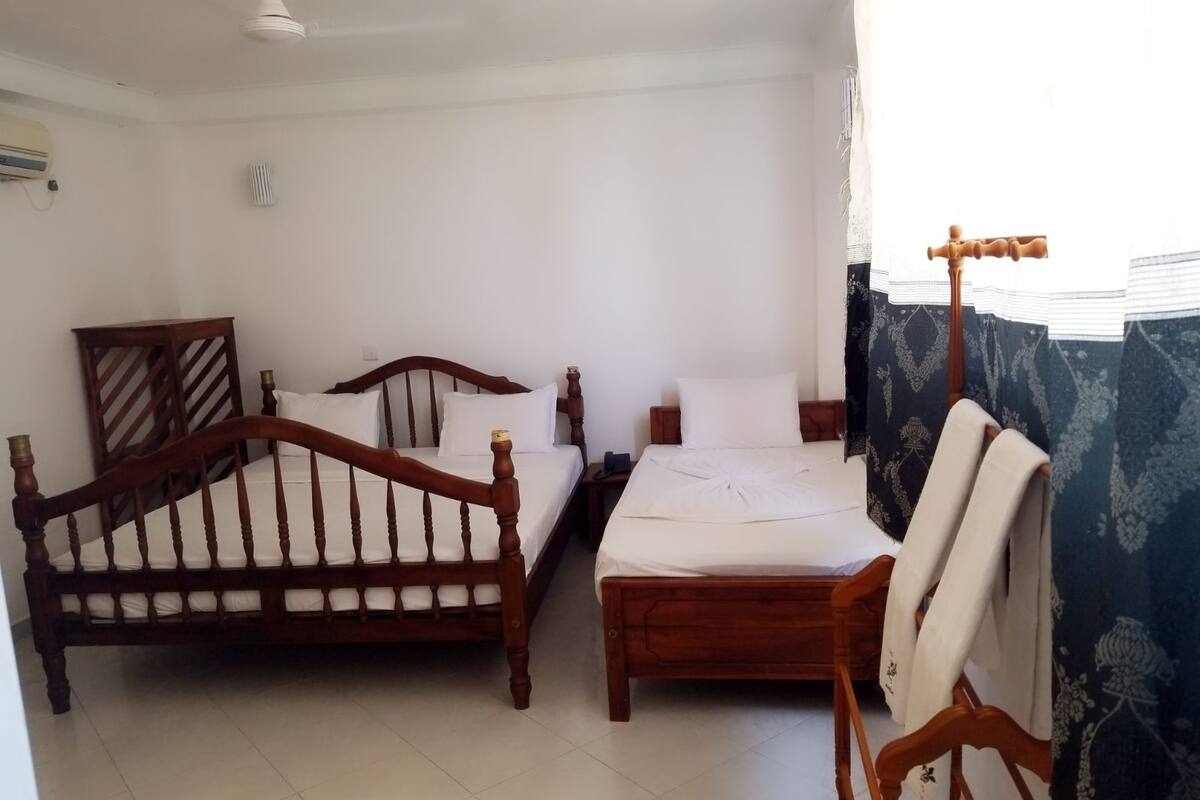 A room with two wooden beds, a ceiling fan, a radiator, and a window with curtains.