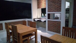 A dining area with a wooden table and chairs, a brick accent wall, and a kitchen area with a sink and countertop visible through an open doorway.