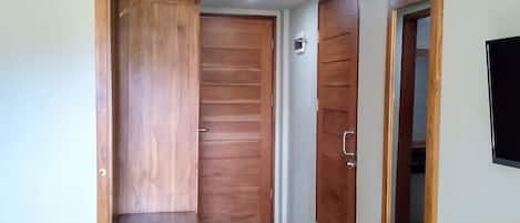 Quarto com cama, guarda-roupa de madeira, pequena mesa de madeira e televisão na parede.