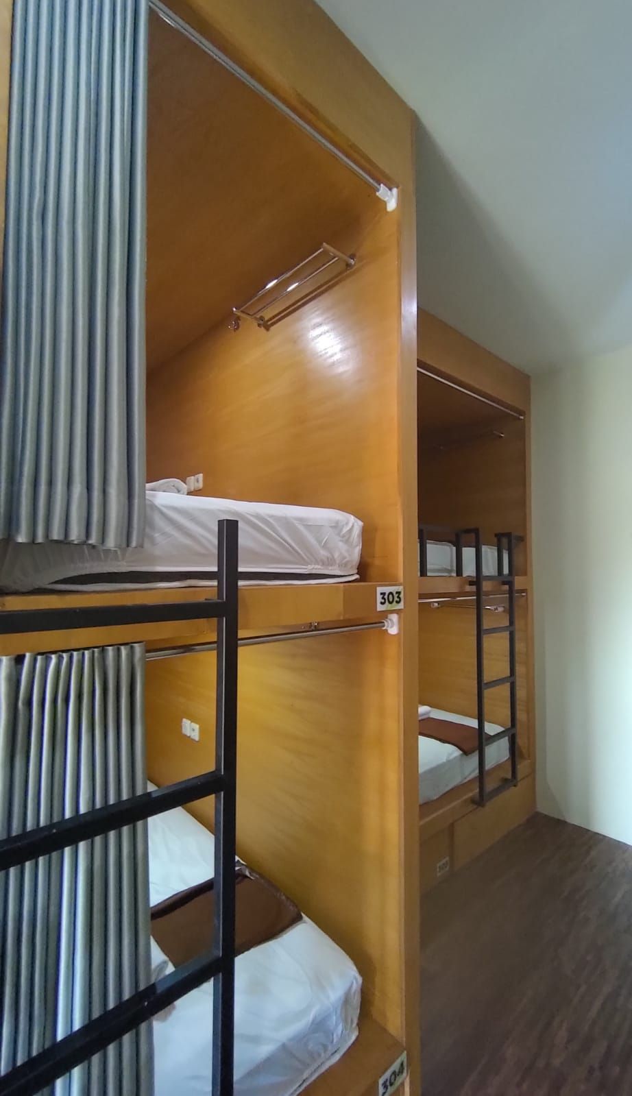 A bunk bed room with wooden bunk beds, numbered 303 and 304, and a curtain on the left side.