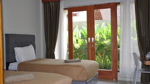 A hotel room with a bed, a chair, and a view of greenery through a sliding door.