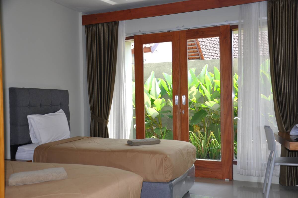 Habitación de hotel con cama, una silla y vista a la vegetación a través de una puerta corredera.