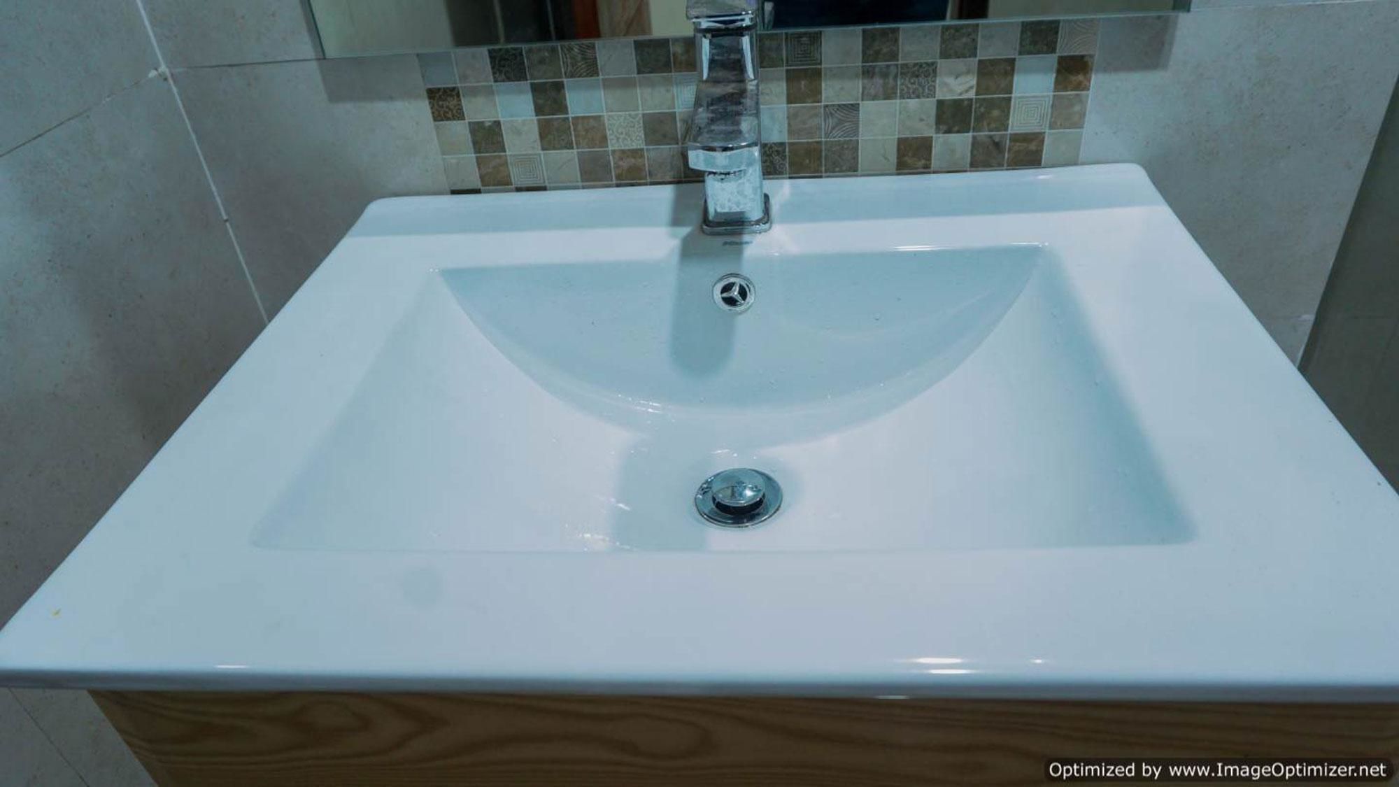 Ein weißes Waschbecken mit einem chromfarbenen Wasserhahn, vor einer gefliesten Rückwand.