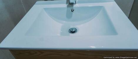 Ein weißes Waschbecken mit einem chromfarbenen Wasserhahn, vor einer gefliesten Rückwand.