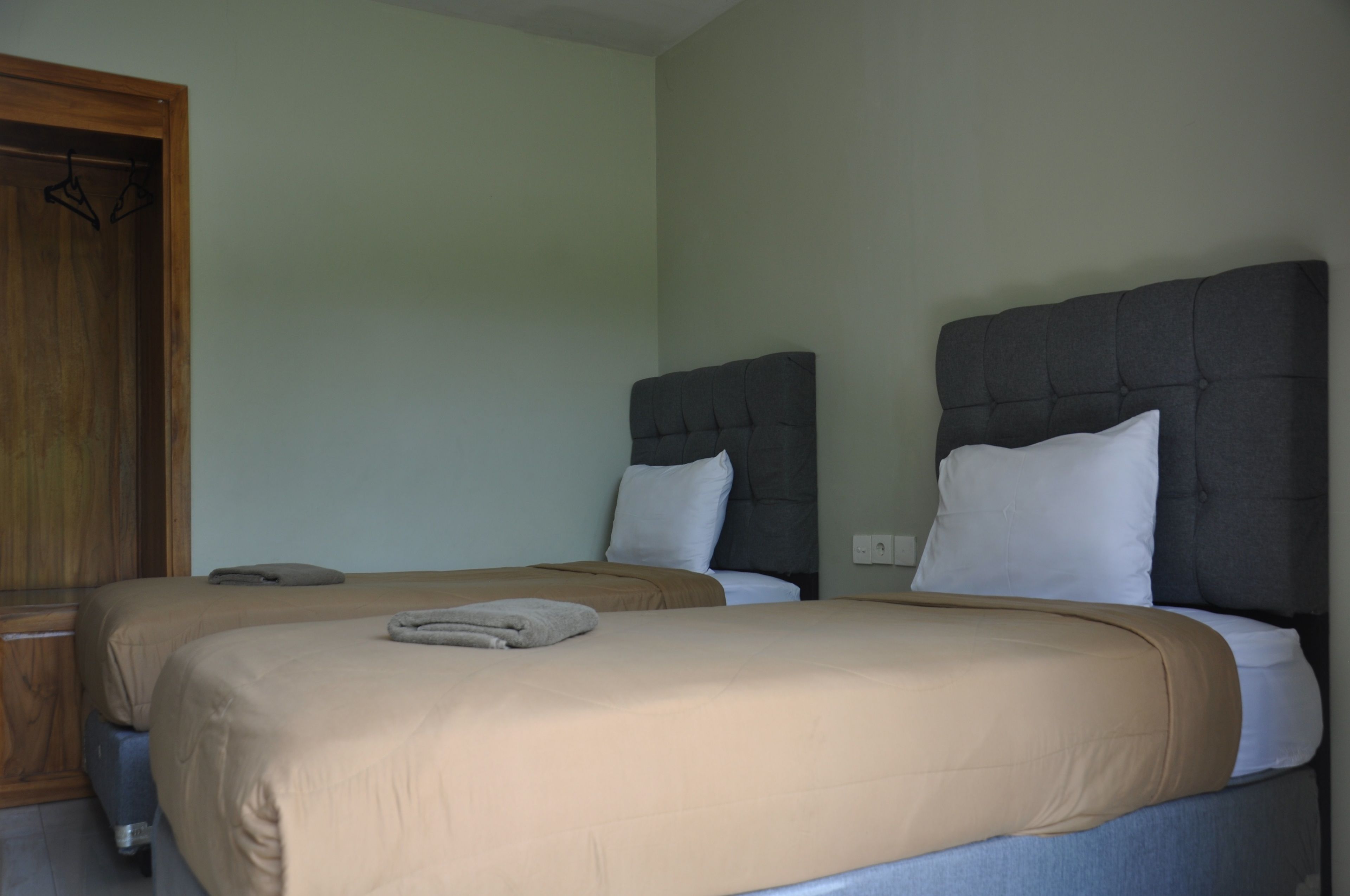 Habitación de hotel con dos camas, cada una con cabecero y almohadas, y un armario de madera.