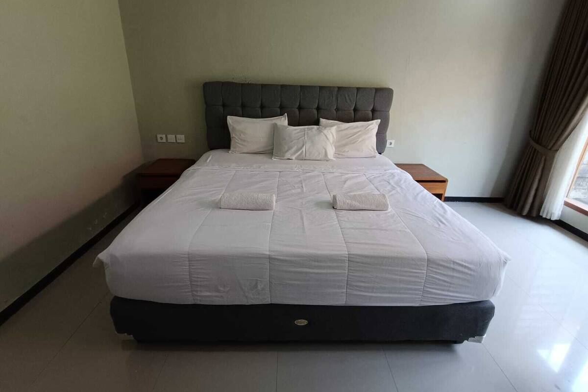 Una cama grande con un cabecero tapizado en gris, ropa de cama blanca y dos mesitas de noche con lámparas.