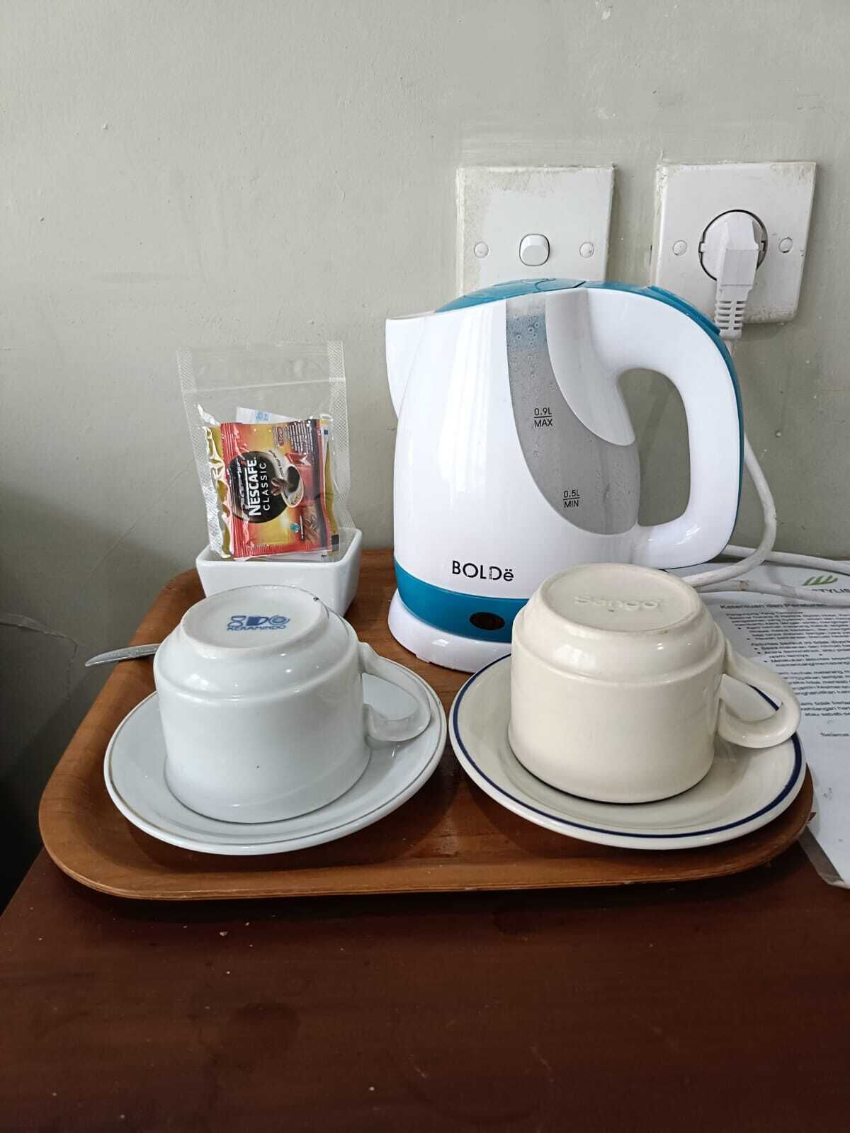 A coffee maker, two cups, and a packet of coffee on a wooden tray.
