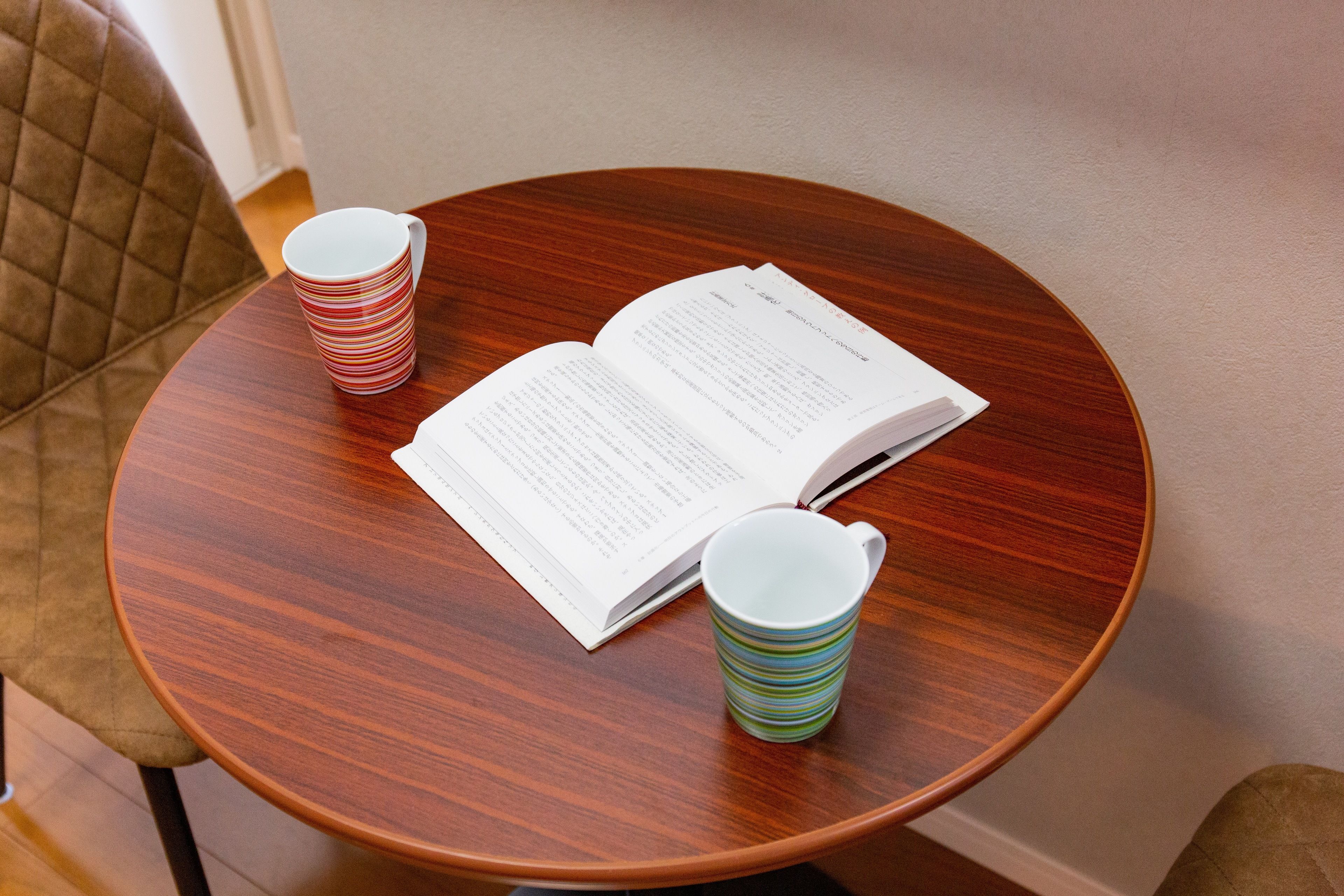 Une table ronde en bois, sur laquelle se trouvent un livre et deux tasses à rayures.