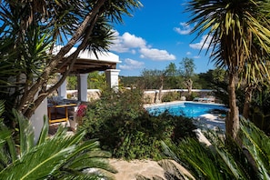 A pool surrounded by lush greenery, a pergola, and a stone wall.
