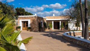 Un edificio de piedra de dos pisos con un patio central, rodeado de abundante vegetación y palmeras.
