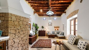 Una sala de estar con pared de piedra, techo de madera, un sofá, una mesa de centro y un tapete estampado.