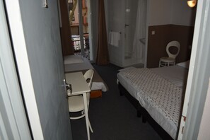A small, compact hotel room with a single bed, a desk with a chair, and a shower area. - Le Charleston Hotel (Rodez)