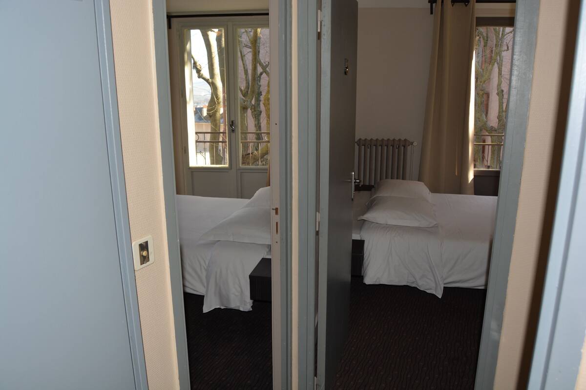 A hotel room with two beds, a radiator, and a window with a view of bare trees.