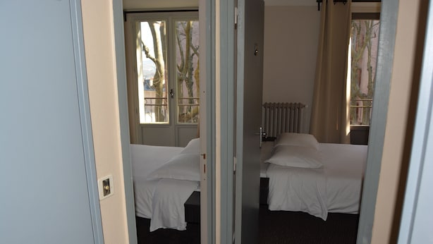 Habitación de hotel con dos camas, un radiador y una ventana que da a árboles desnudos.