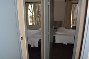 A hotel room with two beds, a radiator, and a window with a view of bare trees. - Le Charleston Hotel (Rodez)