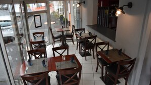 Interior de un restaurante con varias mesas y sillas, puerta de vidrio de entrada y una lámpara fijada a la pared.