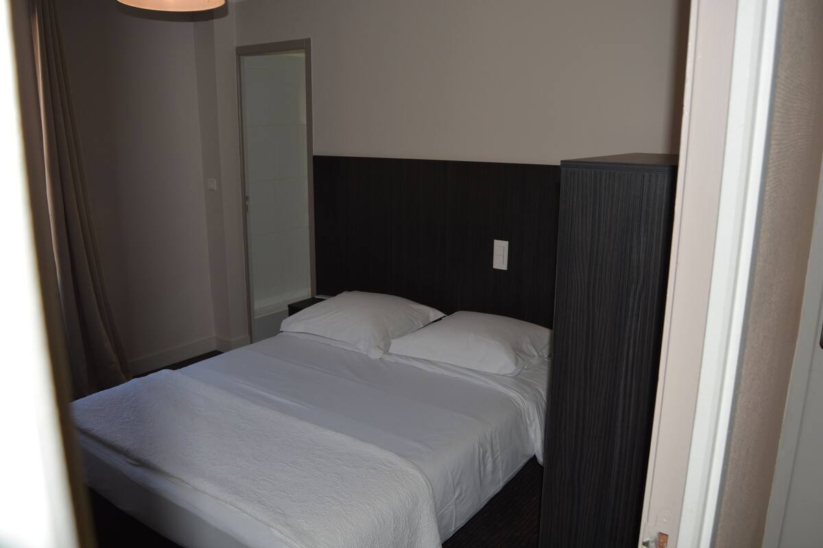 A single bed with white bedding in a room with dark wood paneling and a white door.