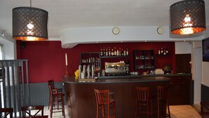 Un área de bar con mostrador curvo, sillas de madera y lámparas colgantes.