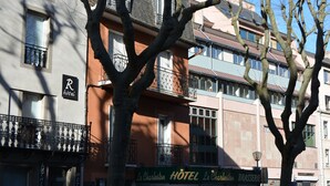 Un hotel con balcones, un cartel que dice 'Le Charleston HOTEL Le Charleston BRASSERIE' y una señalización con la letra 'R' que indica un restaurante.
