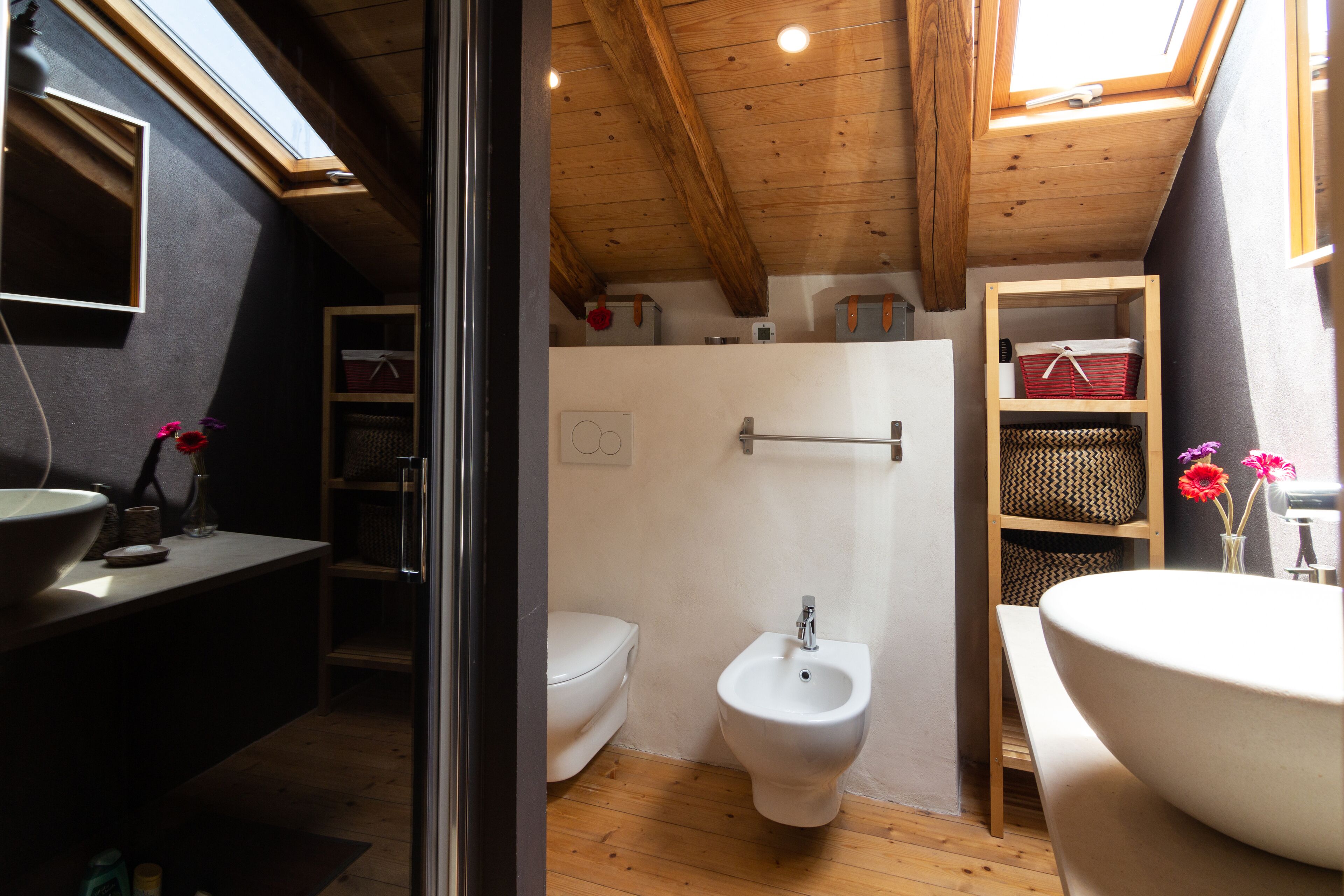 A compact bathroom with a wooden ceiling, a white toilet, a bidet, and a large sink.