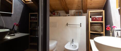 A compact bathroom with a wooden ceiling, a white toilet, a bidet, and a large sink.