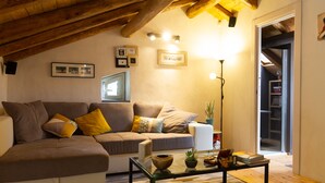 Una sala de estar acogedora con un sofá, una mesita de centro y una estantería. Una escalera conduce a otro nivel.