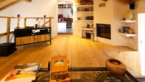 Una sala de estar acogedora con pisos de madera, una chimenea, estanterías y una mesa de centro con un libro y un cofre de madera.